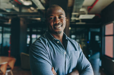 Confident businessman standing in office. African man standing with his arms crossed looking at camera and smiling. - JLPSF13851