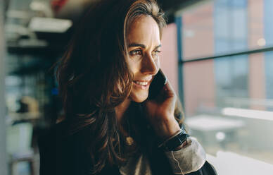 Nahaufnahme einer Geschäftsfrau, die ein Mobiltelefon benutzt und lächelt. Weibliche Führungskraft, die in einem Büro telefoniert. - JLPSF13855
