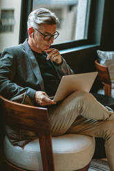 Nachdenklicher Geschäftsmann, der in der Büro-Lobby E-Mails auf seinem Laptop liest. - JLPSF13884