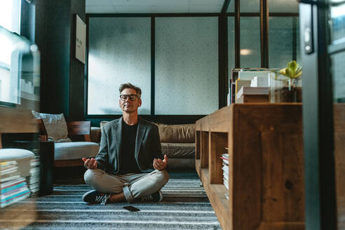 Geschäftsmann meditiert in Lotus-Pose auf dem Boden im Büro. Reife Business-Profi tun Yoga-Meditation im Büro Lounge. - JLPSF13888