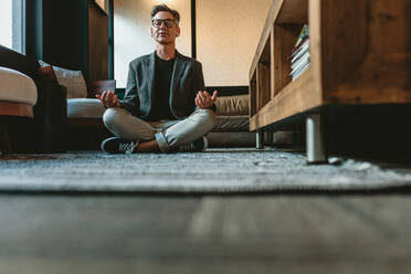 Low angle shot of a mid adult businessman doing yoga meditation. Business professional meditating in yoga pose in office lounge area. - JLPSF13889