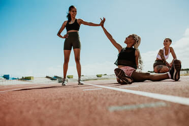 Sportlerinnen machen nach dem Training eine Pause auf der Laufbahn und geben sich im Stadion ein High Five. Eine Gruppe von drei Sprintern entspannt sich nach dem Training auf der Laufbahn. - JLPSF13911