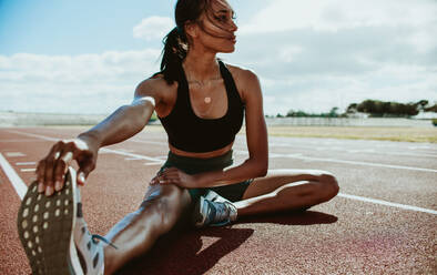 Sportler bei Dehnungsübungen auf der Laufbahn. Eine Läuferin dehnt ihre Beinmuskeln, indem sie ihre Schuhe berührt und wegschaut. - JLPSF13931