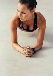 Attractive young woman doing core exercise outdoors on concrete floor. Female doing press-ups exercise. - JLPSF13934