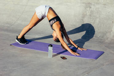 Gesunde Frau beim Yoga am Morgen: Frau in Sportkleidung beim Stretching-Workout im Freien, sie übt die Yoga-Pose des nach unten gerichteten Hundes. - JLPSF13974