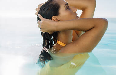 Beautiful young woman standing inside a swimming pool. Female in swimwear in pool on a summer day. - JLPSF14023