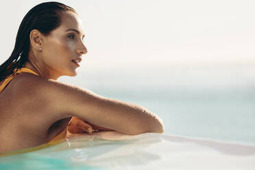 Attraktive junge Frau im Bikini lehnt sich an den Rand des Infinity-Pools. Schöne Frau im Schwimmbad schaut an einem Sommertag weg. - JLPSF14027