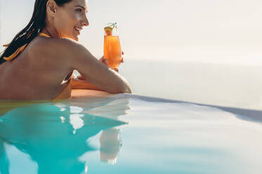 Schöne Frau mit einem Cocktail im Pool. Weibliches Model genießt einen Sommertag in einem Resort-Swimmingpool. - JLPSF14033