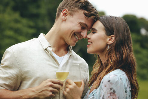 Romantisches Paar im Park mit Champagnergläsern. Mann und Frau stehen zusammen und berühren ihre Stirne mit Champagnergläsern. - JLPSF14068