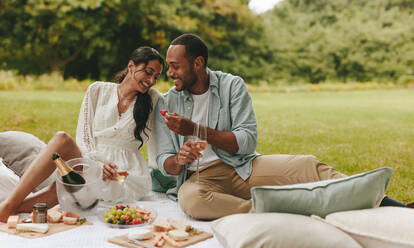 Lächelnder Mann und Frau sitzen auf einer Picknickdecke und essen Erdbeeren und Champagner. Verliebtes Paar beim Picknick. - JLPSF14071