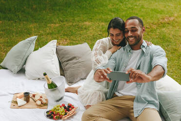 Liebevolles junges Paar, das ein Selfie im Park macht. Schönes Paar beim Picknick, das ein Selbstporträt im Park macht. - JLPSF14073