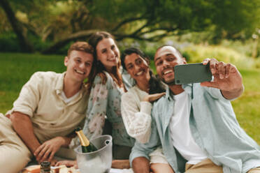 Friends taking selfie with a smart phone at the park. Group of young people on picnic taking a selfie. - JLPSF14075