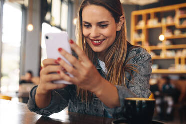 Woman using mobile phone at a cafe. Female sitting at table reading text message on her cellphone. - JLPSF14078