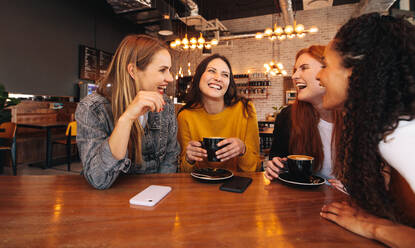 Vier Freundinnen treffen sich am Wochenende in einem Café. Eine Gruppe von Frauen sitzt am Tisch und lächelt. - JLPSF14083