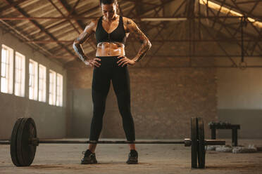 Fitness-Frau steht mit Hanteln auf dem Boden in einem alten Lagerhaus. Eine Sportlerin macht sich bereit, eine Hantel zu heben. - JLPSF14084