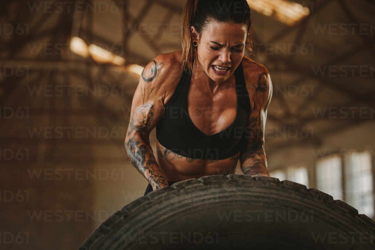 Fitness woman putting effort in flipping a huge tyre at cross