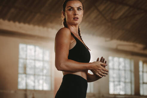 Eine fitte Frau steht nach dem Training in einem verlassenen Lagerhaus. Eine starke Sportlerin in schwarzer Sportkleidung macht nach dem Training eine Pause. - JLPSF14102