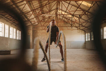 Tough Mann trainiert in Cross-Training Fitnessstudio in alten Fabrik gemacht. Fitness-Mann übt mit Kampf Seil in verlassenen Lagerhalle. - JLPSF14115