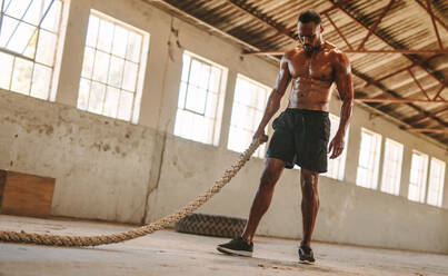 Fitness-Mann mit Kampfseil in altem Lagerhaus. Mann, der sich nach dem Training im Fitnessstudio in einem alten Lagerhaus ausruht. - JLPSF14120