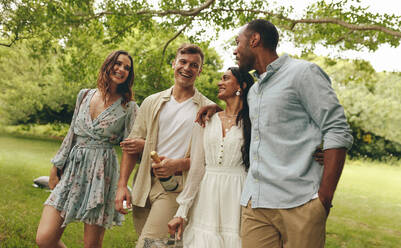 Junge, gemischtrassige Freunde machen ein Picknick im Stadtpark. Eine Gruppe von Männern und Frauen geht mit einer Champagnerflasche im Park spazieren. - JLPSF14142