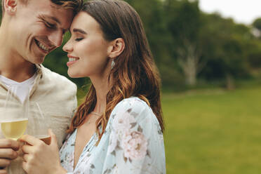 Couple in love with champagne at park. Close-up of affectionate couple standing together holding champagne glasses outdoors. - JLPSF14162