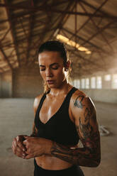 Sportlerin im Fitnessstudio im Schatten einer alten Fabrik. Fitte Frau steht nach dem Training in einem verlassenen Lagerhaus. - JLPSF14193