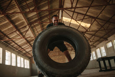 Starker Mann macht ein Reifenflip-Training in einem alten Lagerhaus. Mann macht Cross-Training. - JLPSF14210