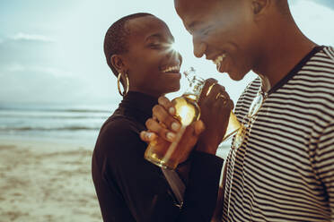 Schönes verliebtes Paar beim Biertrinken am Strand. Lächelnder junger Mann und Frau stehen am Strand und trinken Bier. - JLPSF14261