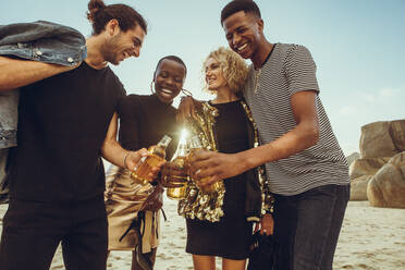 Multi-ethnic group of friends at the beach having beers. Young men and woman at the beach toasting beers. - JLPSF14265