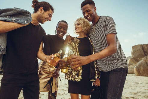 Multiethnische Gruppe von Freunden am Strand, die ein Bier trinken. Junge Männer und Frauen am Strand, die mit einem Bier anstoßen. - JLPSF14265