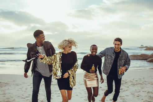 Eine Gruppe von vier jungen Leuten, die sich am Strand amüsieren. Eine multiethnische Gruppe von Männern und Frauen, die am Strand laufen und Spaß haben. - JLPSF14273