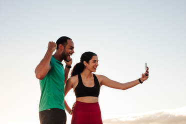 Fröhliches, sportliches Paar, das sich nach dem Training vergnügt. Fitness-Frau macht ein Selfie im Freien mit ihrem Laufpartner. - JLPSF14291