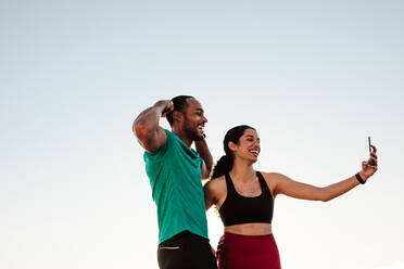 Smiling woman taking a selfie with her running mate. Young fitness couple relaxing after workout taking a selfie outdoors. - JLPSF14292