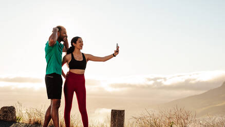 Fitness-Paar steht im Freien und macht ein Selfie nach dem Training. Ein Paar, das sich nach einem Lauf entspannt und ein Selfie mit dem Handy macht. - JLPSF14293