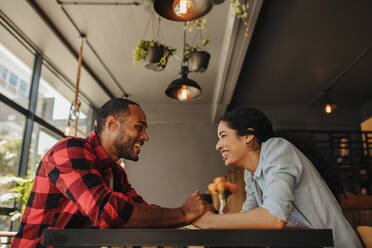 Cheerful couple sitting at cafe holding hands. Man and woman sitting at restaurant table looking at each other and smiling. - JLPSF14303