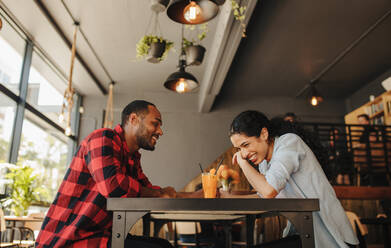 Happy couple sitting at cafe table with a glass of juice. Couple in love talking and smiling at a coffee shop. - JLPSF14308