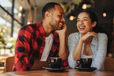 Beautiful couple sitting together at coffee shop and smiling. Man and woman sitting at cafe tablet with cups of coffee. - JLPSF14310
