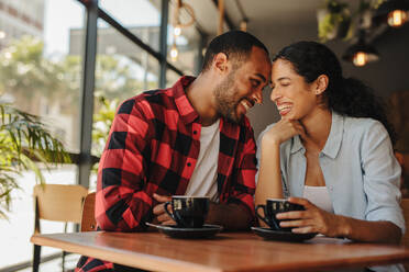 Verliebtes Paar genießt ihr Date in einem Café. Lächelnder Mann und lächelnde Frau sitzen im Café und berühren sich an der Stirn. - JLPSF14311