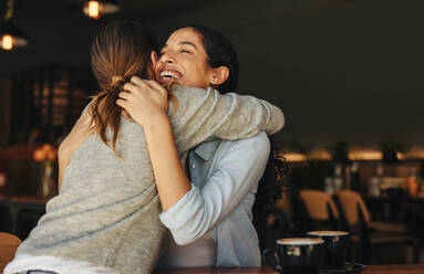 Fröhliche Freundinnen, die sich in einem Café umarmen und begrüßen. Zwei Frauen treffen sich in einem Café und umarmen sich. - JLPSF14319