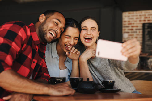 Frau nimmt Selfie mit Freunden in einem Café. Freunde im Café haben Spaß und nehmen Selfies. - JLPSF14322