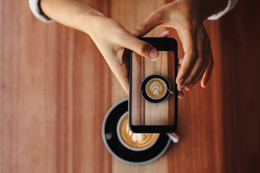 Hand einer Frau, die einen Kaffee mit ihrem Mobiltelefon fotografiert. Nahaufnahme einer Frau, die ihren Kaffee mit einem Smartphone fotografiert. - JLPSF14327