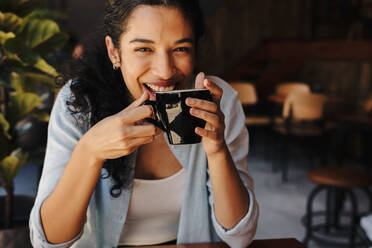 Schöne Frau sitzt im Café mit einer Tasse Kaffee und lächelt. Afrikanische Frau trinkt Kaffee im Café. - JLPSF14329