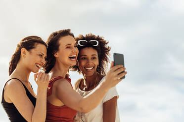 Porträt von drei Freundinnen, die ein Selfie im Freien machen. Glückliche Frau, die ein Selfie mit ihren Freundinnen mit dem Handy macht. - JLPSF14335