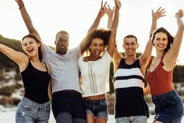 Cheerful group of friends enjoying their vacation. Multiethnic friends standing together with arms raised having fun. - JLPSF14336