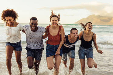 Glückliche junge Freunde, die im Meer laufen und sich gegenseitig festhalten. Gruppe von Männern und Frauen, die sich im Urlaub am Meer vergnügen. - JLPSF14342