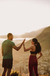 Fitness couple giving a high five after workout standing on a hill. Athletic man and woman celebrate after a run. - JLPSF14349