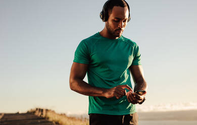 Portrait of an athlete using mobile phone during morning run. Athletic man listening to music on wireless headphones. - JLPSF14353