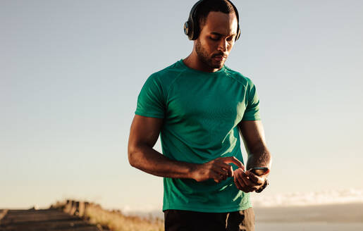 Porträt eines Sportlers, der beim morgendlichen Lauf sein Mobiltelefon benutzt. Ein sportlicher Mann hört Musik über drahtlose Kopfhörer. - JLPSF14353