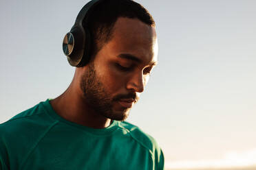 Portrait of an african american athlete wearing a wireless headphones. Close up of a fitness man standing outdoors listening to music. - JLPSF14354