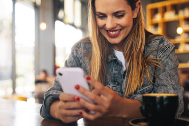 Frau, die sich im Café entspannt und ihr Telefon benutzt. Lächelnde Frau, die im Café sitzt und Social-Media-Updates überprüft. - JLPSF14358